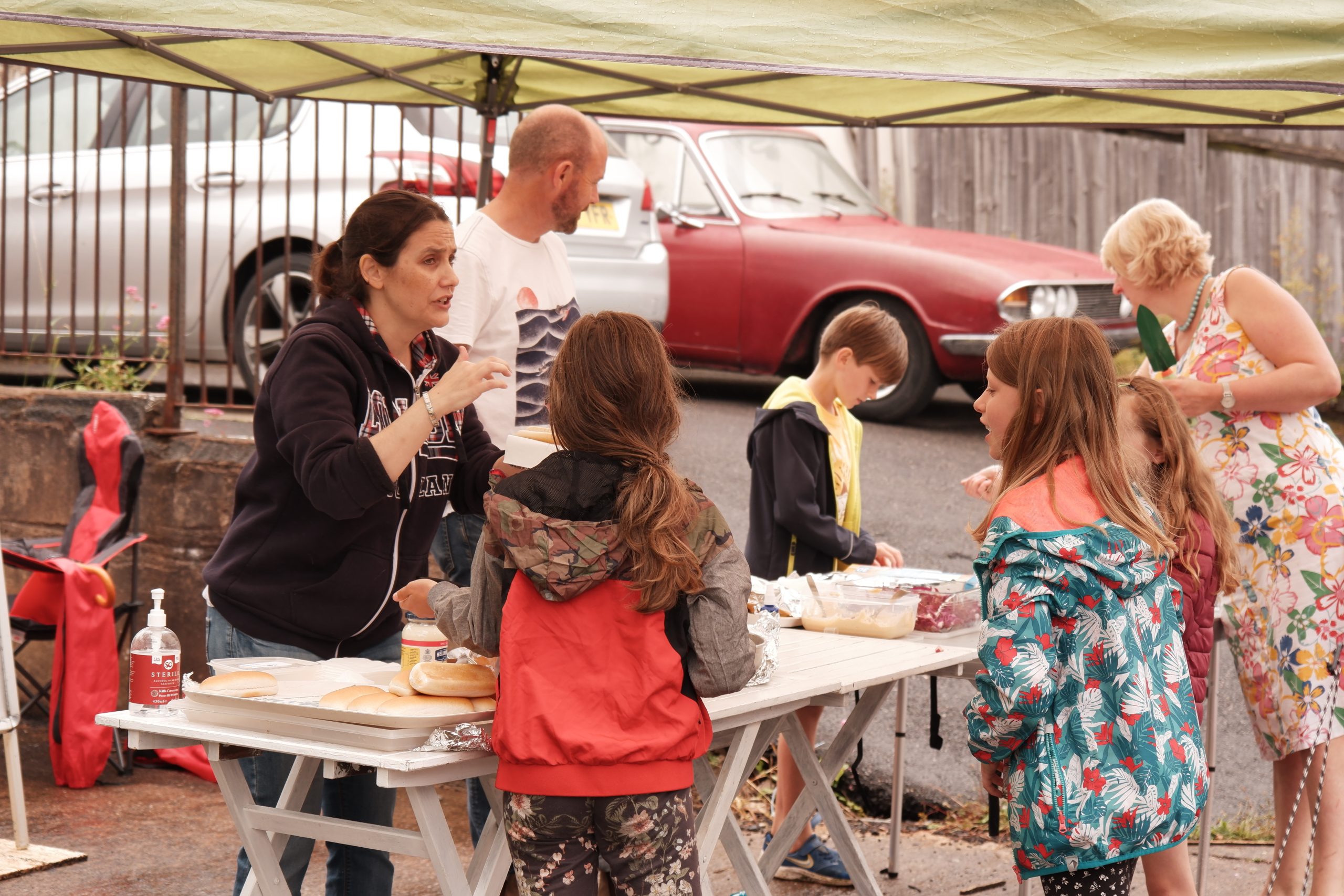 A group of 3 children and 2 adults around a table set up for making hot dogs